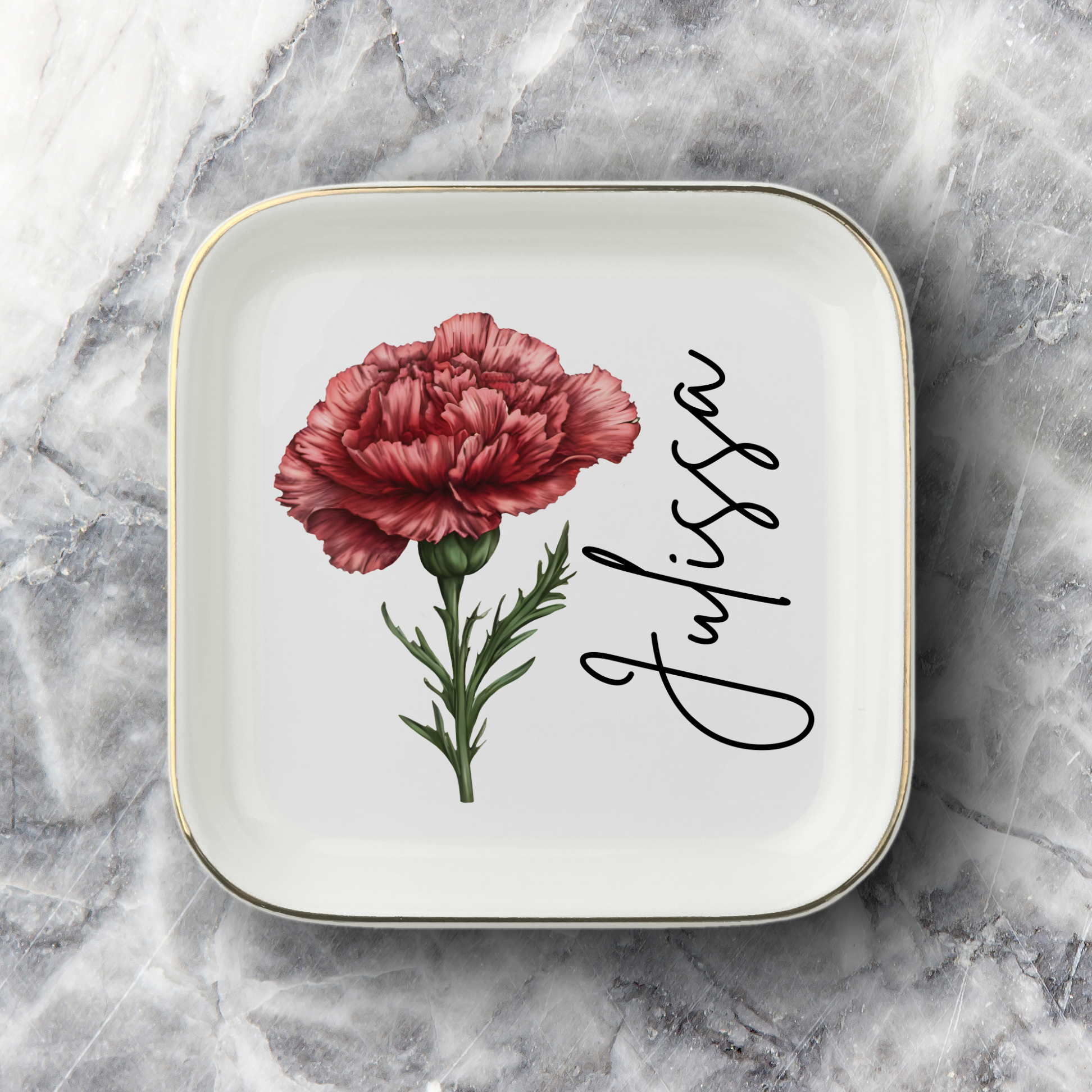 A square white ceramic plate with rounded corners, featuring a red carnation flower illustration and the name 'Julissa' in black cursive script, set against a gray marble background.