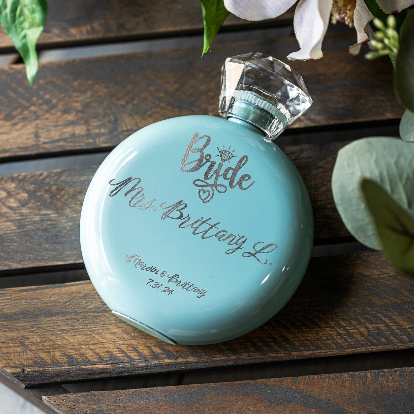 A round light blue flask with a faceted clear cap, engraved with custom text 'Bride Mrs. Brittany L.