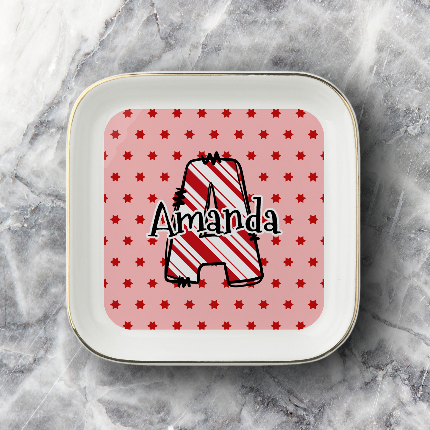 A square white ceramic plate with rounded corners and a thin gold rim, featuring a personalized design. The center has a pink background with small red stars and a large outlined letter 'A' filled with red and white diagonal stripes, with the name 'Amanda' written across it in black script.