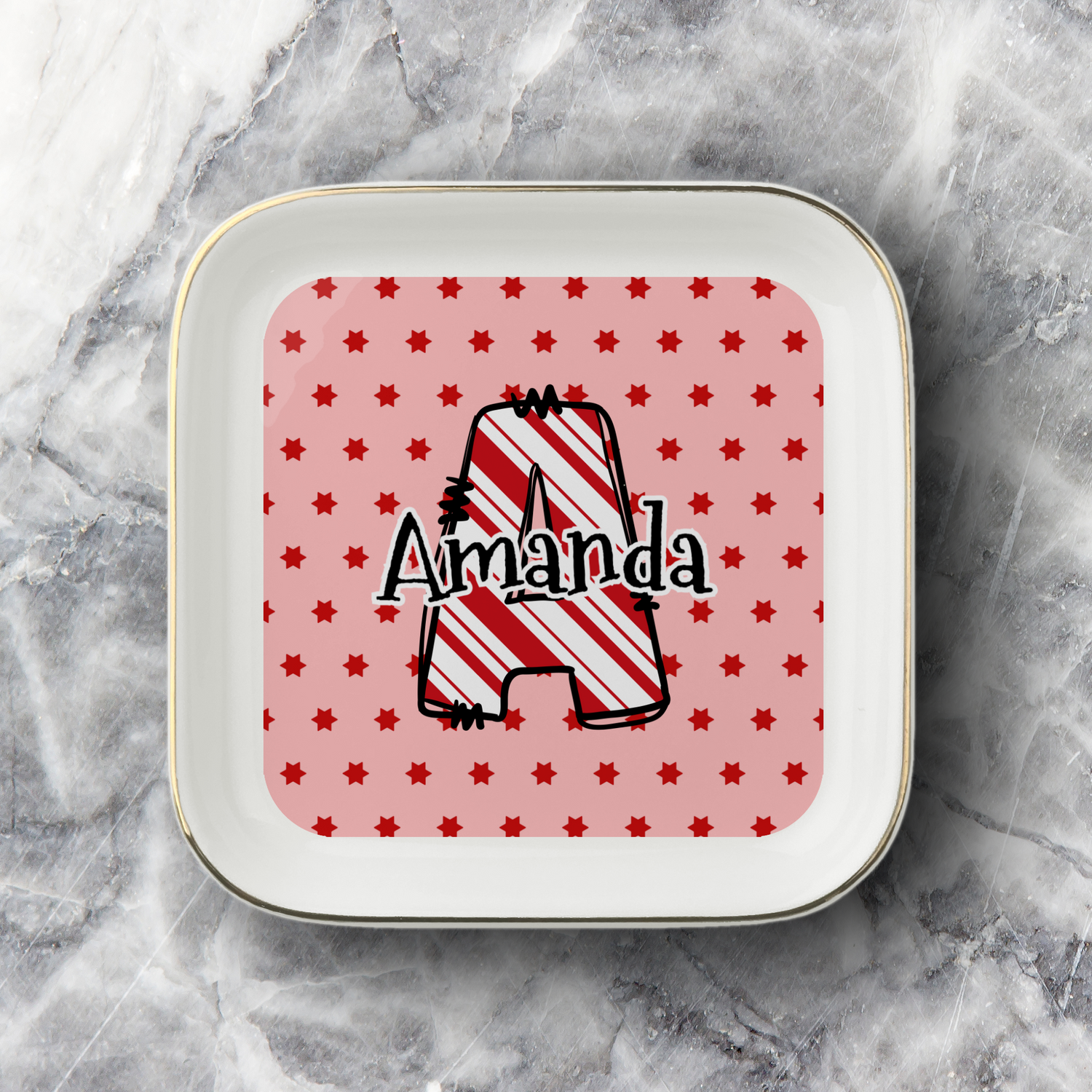 A square white ceramic plate with rounded corners and a thin gold rim, featuring a personalized design. The center has a pink background with small red stars and a large outlined letter 'A' filled with red and white diagonal stripes, with the name 'Amanda' written across it in black script.