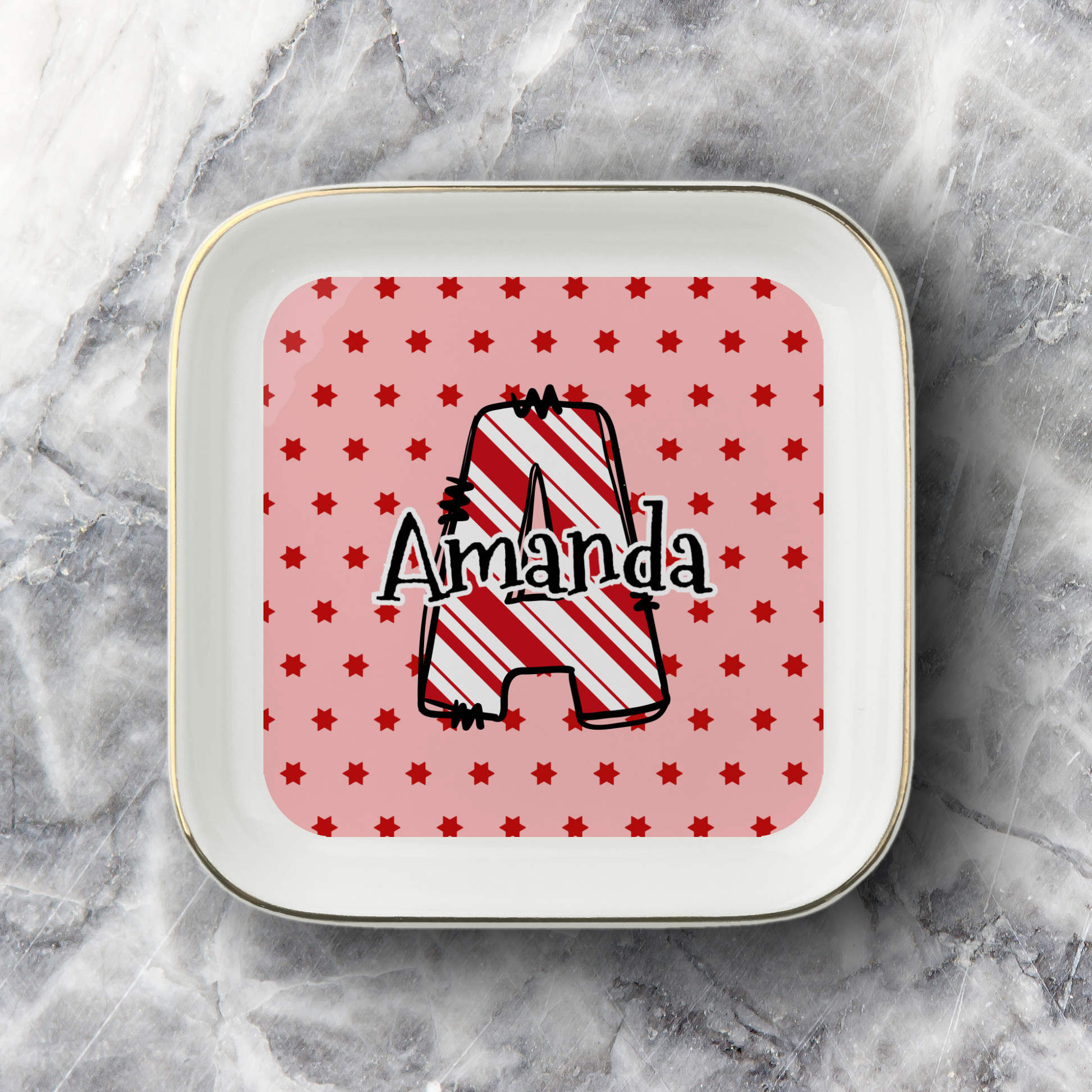 A square white ceramic plate with rounded corners and a thin gold rim, featuring a personalized design. The center has a pink background with small red stars and a large outlined letter 'A' filled with red and white diagonal stripes, with the name 'Amanda' written across it in black script.