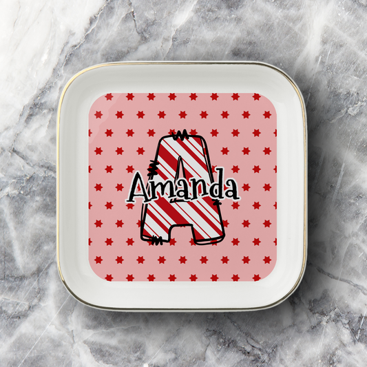 A square white ceramic plate with rounded corners and a thin gold rim, featuring a personalized design. The center has a pink background with small red stars and a large outlined letter 'A' filled with red and white diagonal stripes, with the name 'Amanda' written across it in black script.