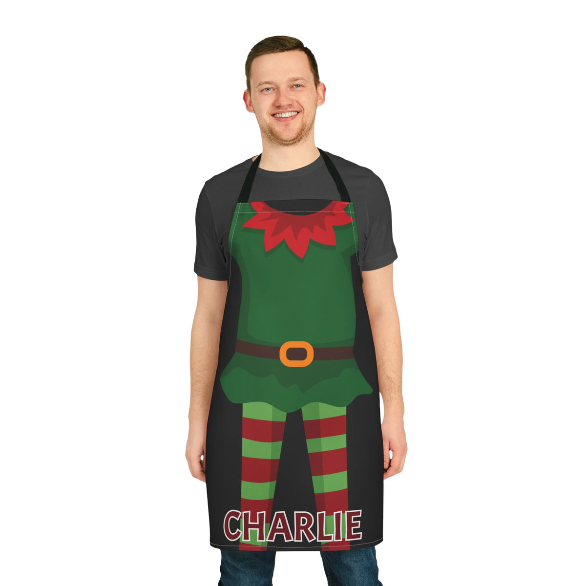 A man wearing a black kitchen apron with a festive elf costume graphic and the name 'CHARLIE' printed at the bottom, shown against a plain white background.