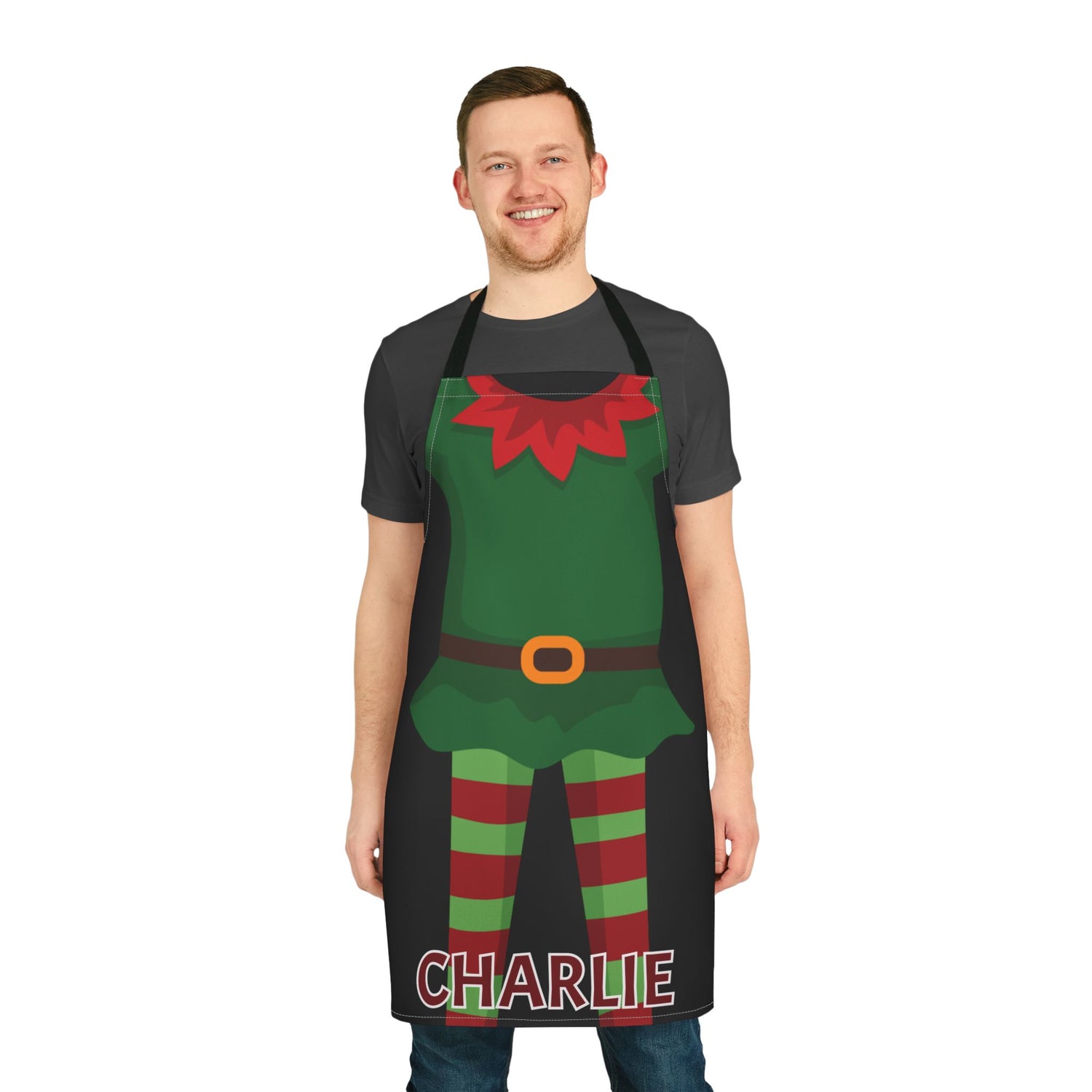 A man wearing a black kitchen apron with a festive elf costume graphic and the name 'CHARLIE' printed at the bottom, shown against a plain white background.