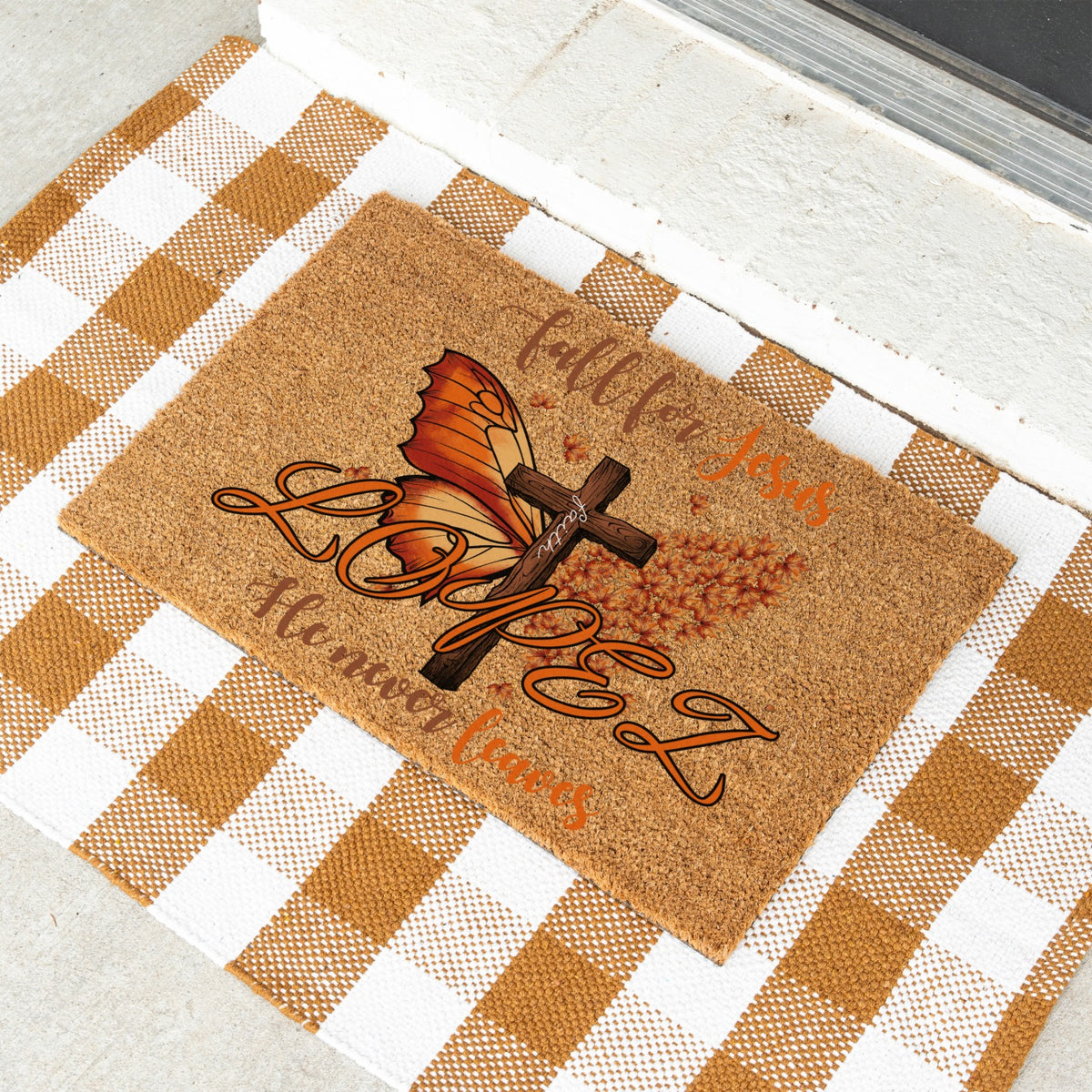 A rectangular cork doormat with a fall-themed graphic featuring a butterfly, cross, and the words 'Fall For Jesus' and 'He Never Leaves'  with the custom name 'Lopez' and its placed on a white and tan checkered blanket.