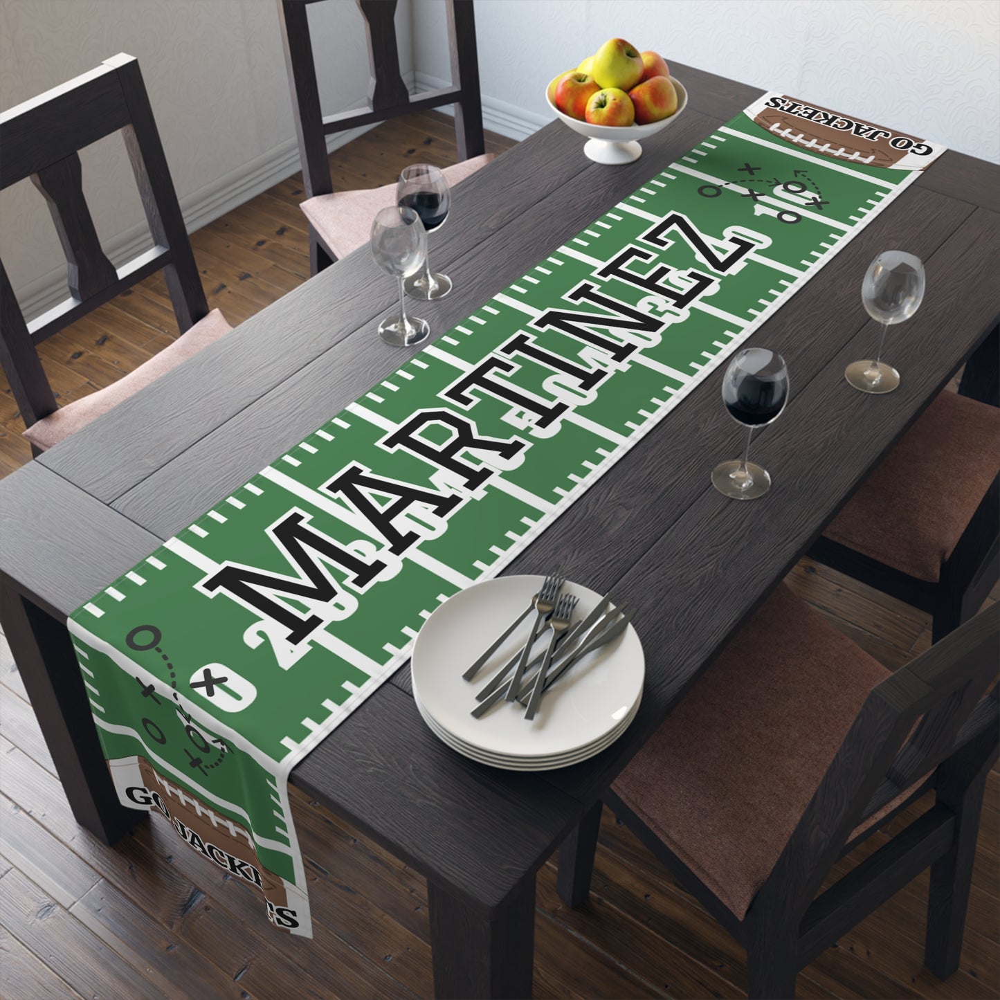 A green and white football field themed table runner with the custom name 'MARTINEZ' in large black letters, styled on a dark wooden dining table with plates, wine glasses, and chairs.