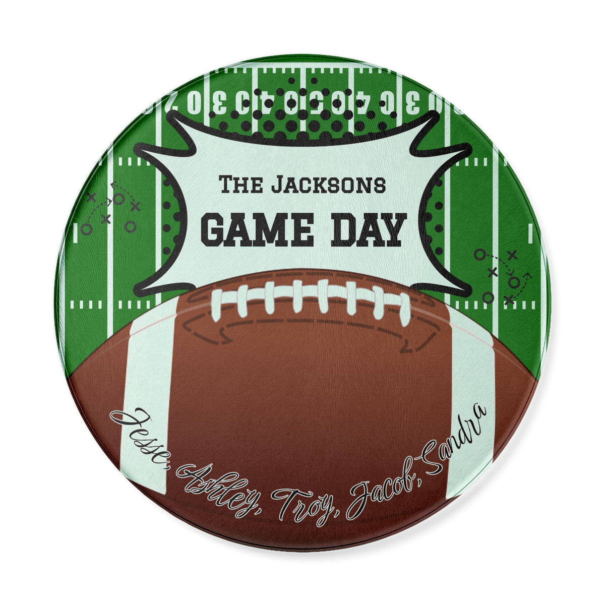 A round custom football-themed cutting board featuring a brown football on a green field background with white yard lines. A white banner across the top reads 'THE JACKSONS GAME DAY' in black text, and the bottom shows custom names cursive text.