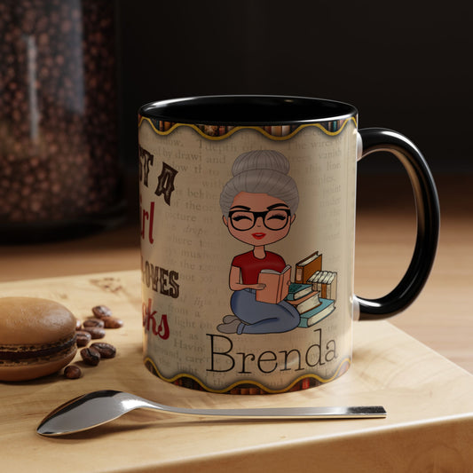 A personalized ceramic mug with a black handle and interior, featuring a cartoon illustration of a woman reading and the custom name 'Brenda' printed on a beige book-textured background. The mug sits on a wooden surface next to a spoon, coffee beans, and a macaron.