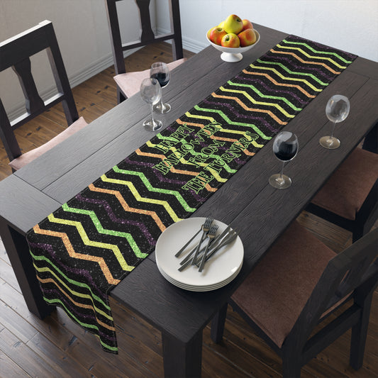 Dining table with a halloween colored zigzag / chevron pattern that looks glittery but its not table runner that has custom wording that reads HAPPY HALLOWEEN FROM THE TURNERS. There are plates, and glasses on a brown table.