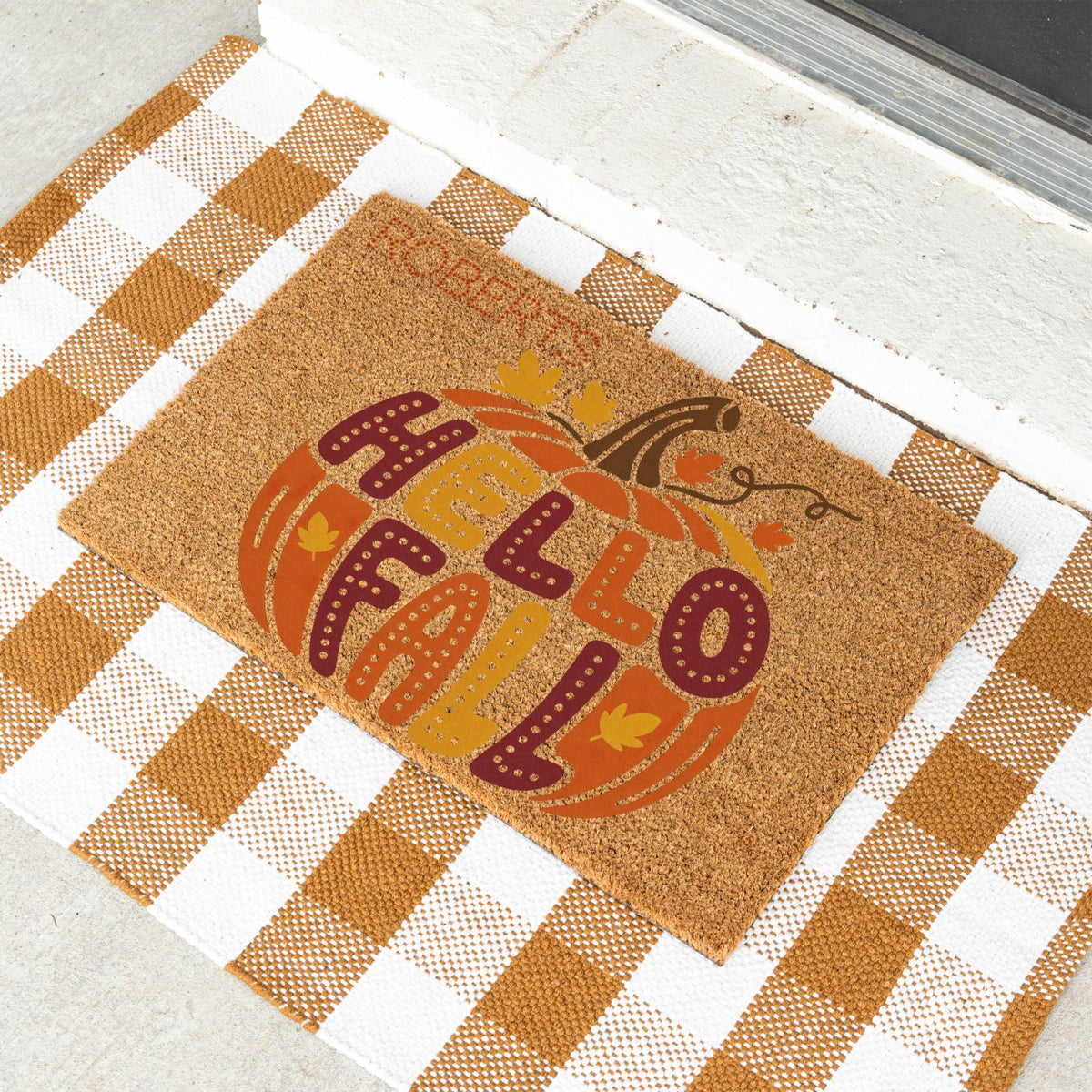 A doormat with a pumpkin and the words HELLO FALL is in the middle of the pumpkin. The custome name ROBERTS in on the top left corner
