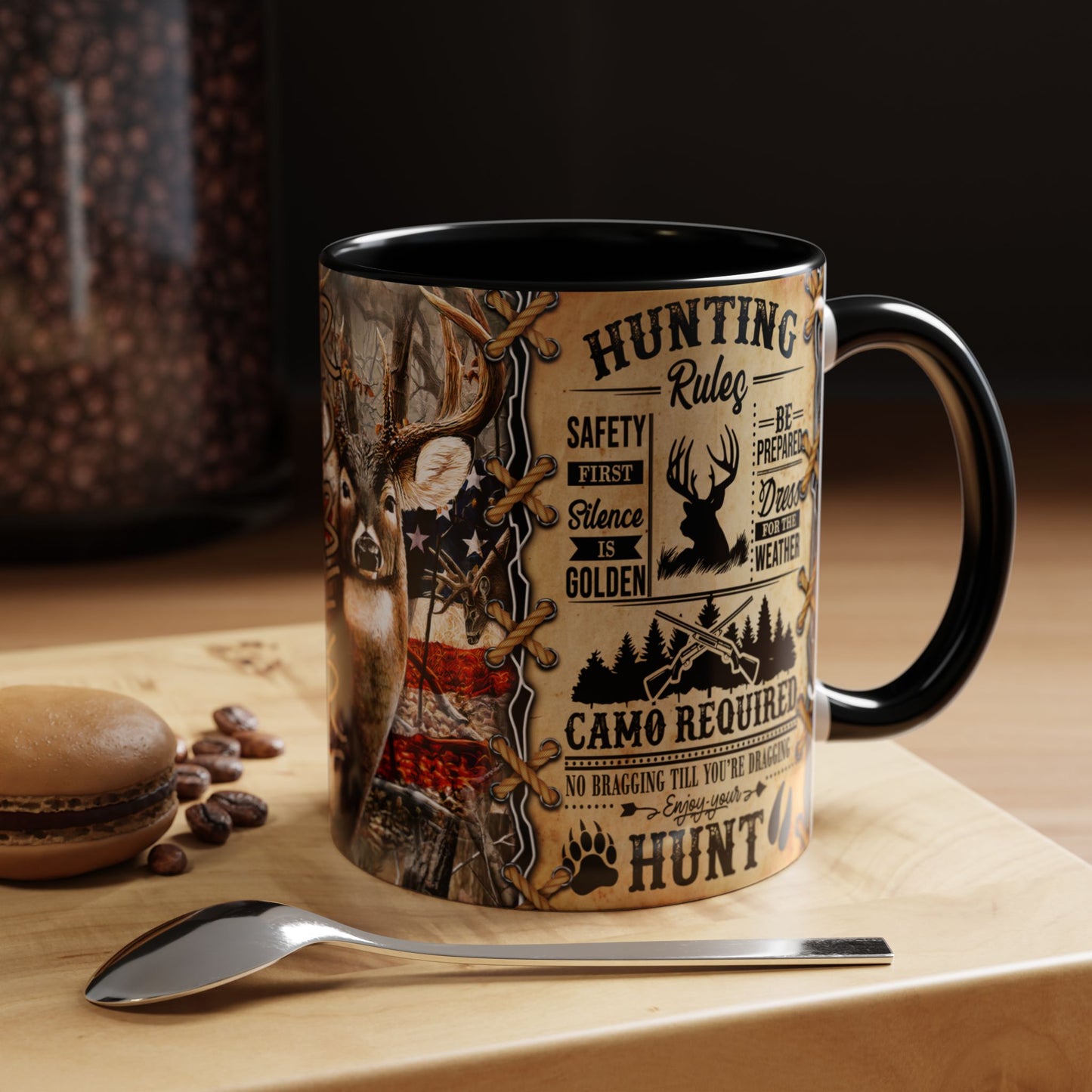 A ceramic coffee mug with a black handle and interior, featuring a detailed hunting-themed graphic print on a light wood surface with a spoon and coffee beans nearby.