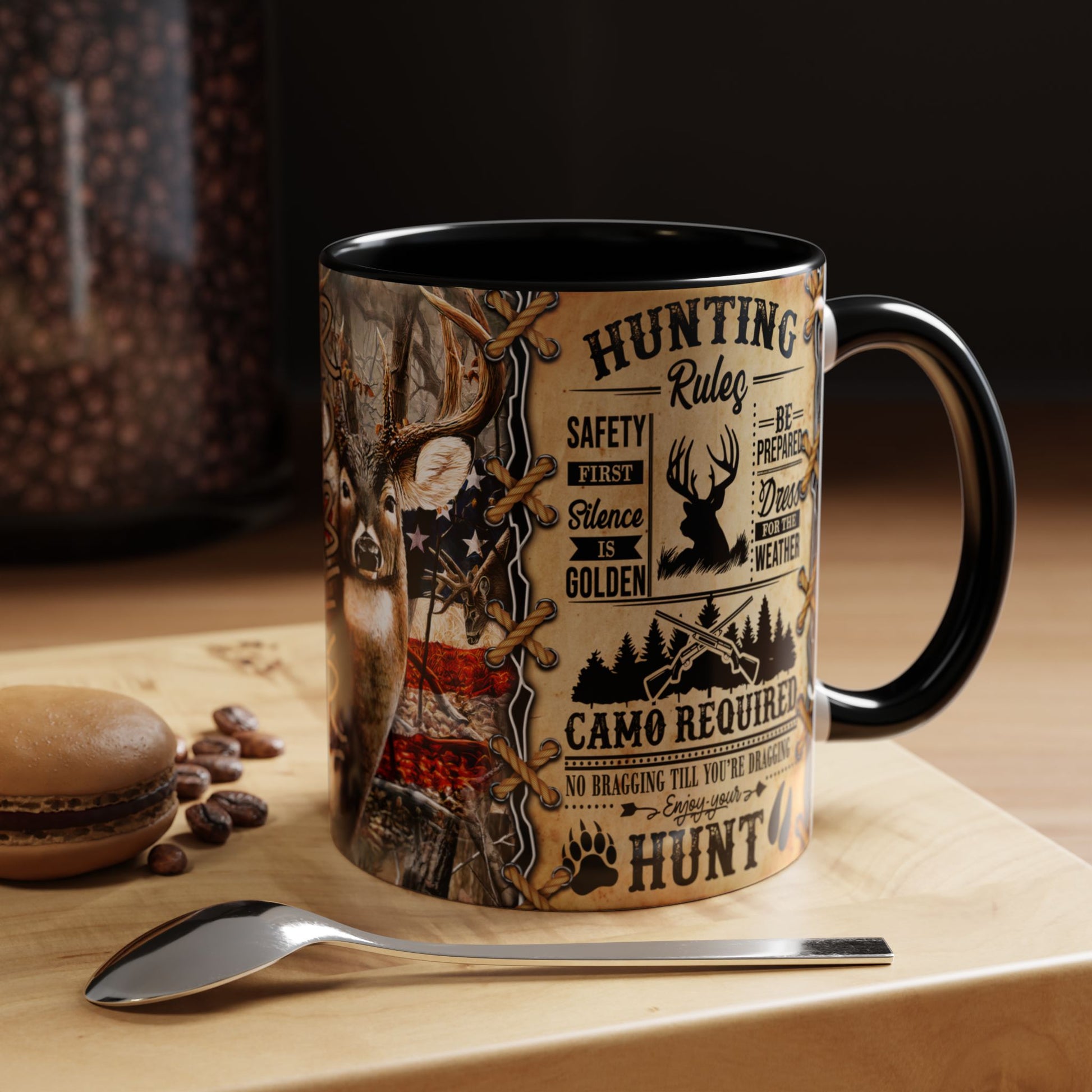 A ceramic coffee mug with a black handle and interior, featuring a detailed hunting-themed graphic print on a light wood surface with a spoon and coffee beans nearby.
