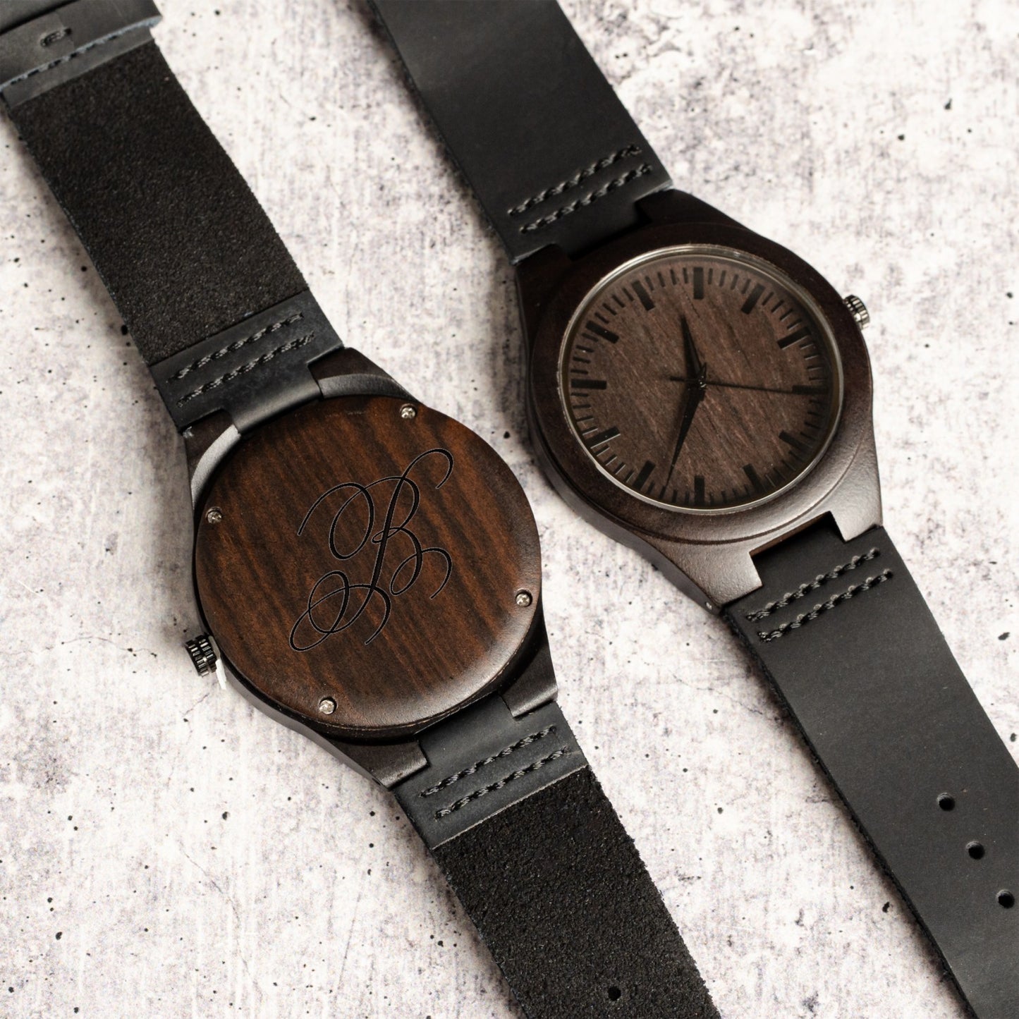 Two wooden watches with custom engraved initial on a textured surface