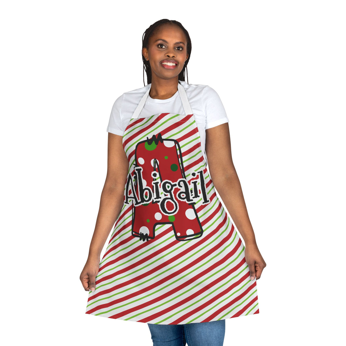 A woman modeling a personalized kitchen apron with a red and green striped pattern, featuring a red polka-dot Christmas custom Letter A graphic with the custom name 'Abigail' written across it.