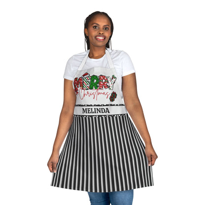 A woman modeling a personalized Christmas apron with a black and white striped skirt portion, a white bib section, and a festive 'Merry Christmas' graphic. The custom name 'MELINDA' is printed on the waistband.