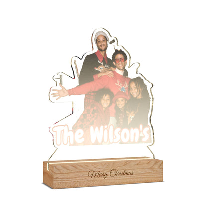 Personalized acrylic LED light sign shaped like a family portrait, featuring a photo of a man and children with the text 'The Wilson's' and a wooden base engraved with 'Merry Christmas'.