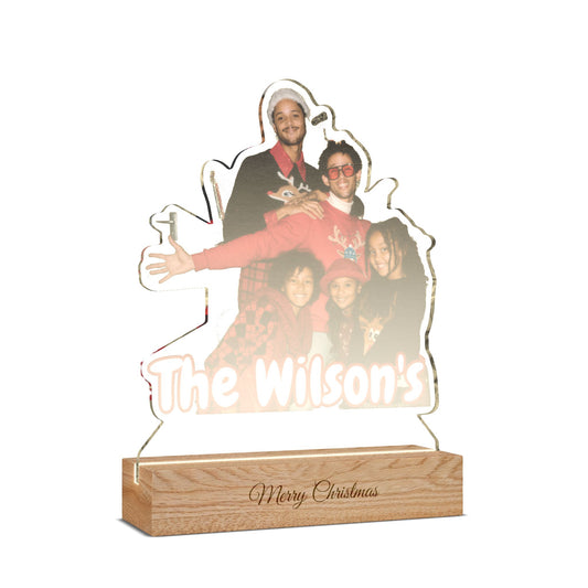 Personalized acrylic LED light sign shaped like a family portrait, featuring a photo of a man and children with the text 'The Wilson's' and a wooden base engraved with 'Merry Christmas'.
