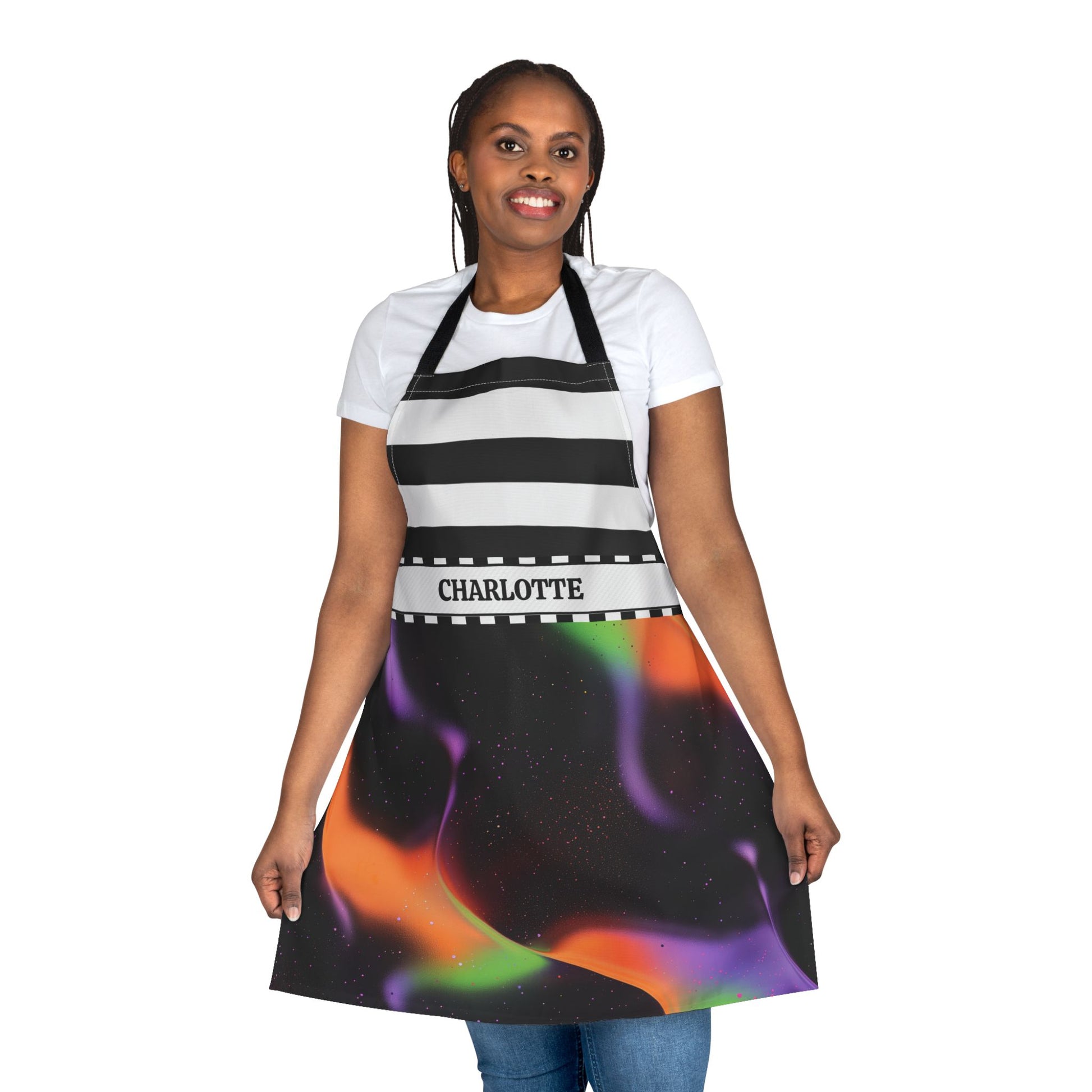 A woman modeling a personalized kitchen apron with a black and white striped upper section and a colorful aurora borealis print on a black background. The apron features the name 'CHARLOTTE' printed on a white band around the waist.