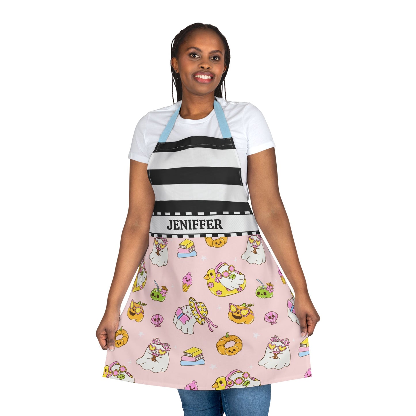 A woman modeling a custom kitchen apron with a black and white striped upper section and a pink lower skirt printed with cartoon ghosts, donuts, and cakes. The waistband is white with the name 'JENIEFFER' printed in black.
