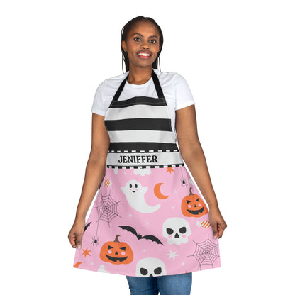 A woman modeling a Halloween-themed kitchen apron over a white t-shirt and jeans. The apron features a black and white striped upper section with the name 'JENIFFER' printed on the waistband, and a pink lower section decorated with cartoon ghosts, pumpkins, skulls, bats, and spiderwebs.