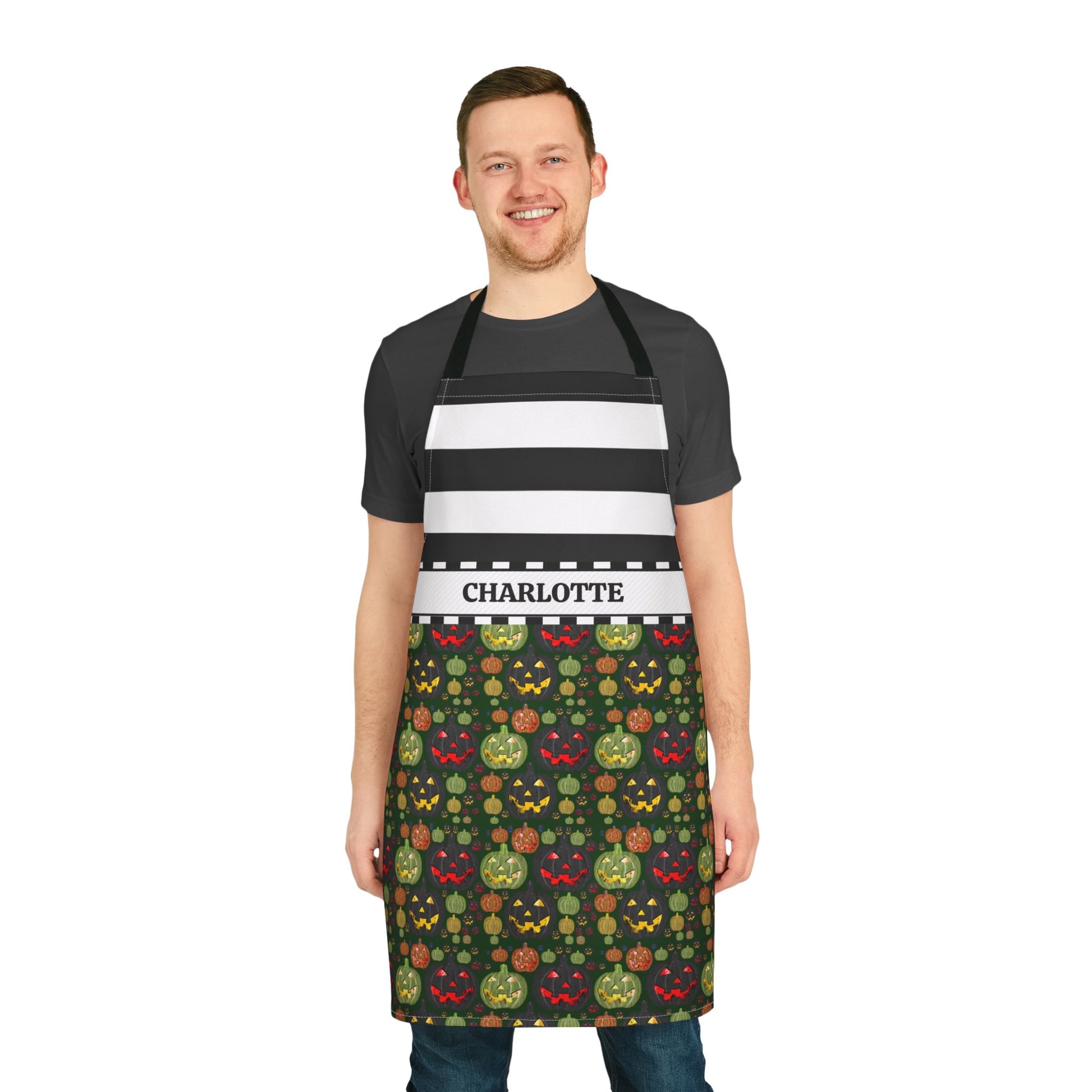 A man wearing a black and white striped apron with a personalized name band reading 'CHARLOTTE' and a dark green Halloween-themed patterned lower section, standing against a plain white background.