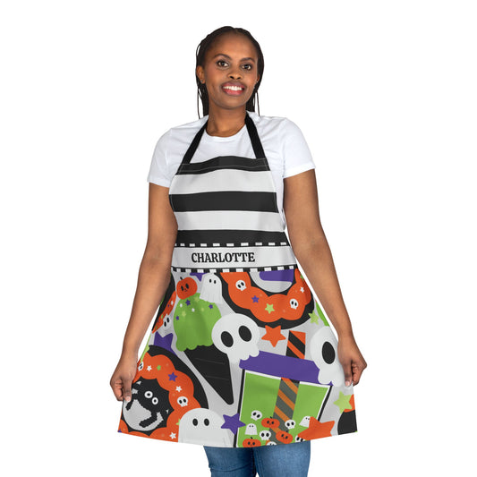 A woman modeling a black and white striped apron with a colorful Halloween-themed print featuring ghosts, pumpkins, and stars. The apron has a waistband with the name 'CHARLOTTE' printed on it.