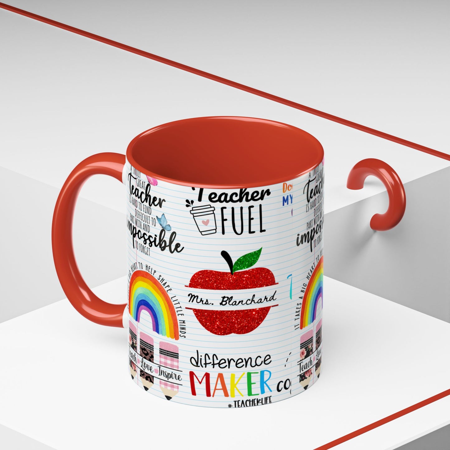 A ceramic mug with a red interior and handle, featuring a white paper printed wrap design with black text, a red glittery apple, rainbows, and the phrase 'Teacher Fuel' amongst other teacher designs on a clean white studio background