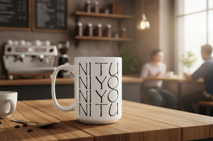 White mug with black text that says ni tu ni yo on a table in a coffee shop