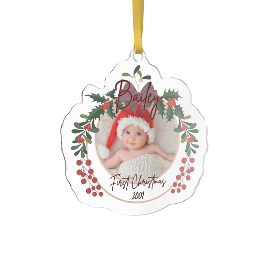 A personalized acrylic Christmas ornament with a scalloped edge, featuring a photo of a baby in a Santa hat surrounded by holly leaves and red berries. The custom name 'Bailey' is written at the top in cursive, and custom text 'First Christmas 2001' is written at the bottom.