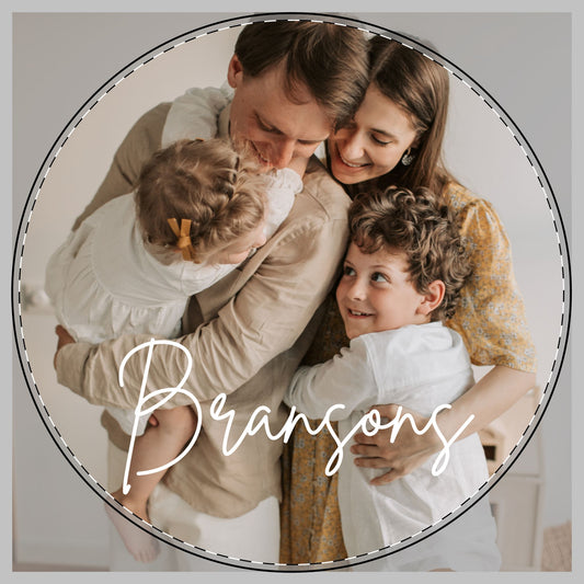 A circular family portrait and the word 'Bransons' in white script across the bottom, showing a father, mother, and two children in a warm indoor setting to be on a custom cutting board.
