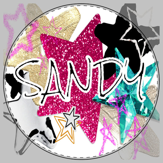 A circular graphic design featuring the word 'SANDY' in white outlined lettering over a glittery pink star, surrounded by layered star shapes in gold, black, teal, gray, and white on a white background. This design goes on a cutting board here.