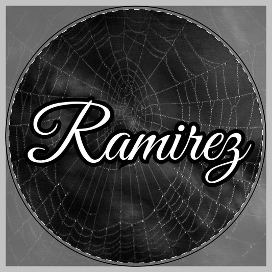 A circular black and white graphic featuring a spiderweb pattern with the name 'Ramirez' written across the center in large white cursive script with a black outline for a citting board.